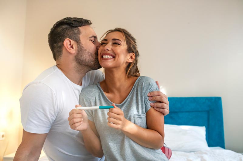 couple sitting on bed smiling with pregnancy test