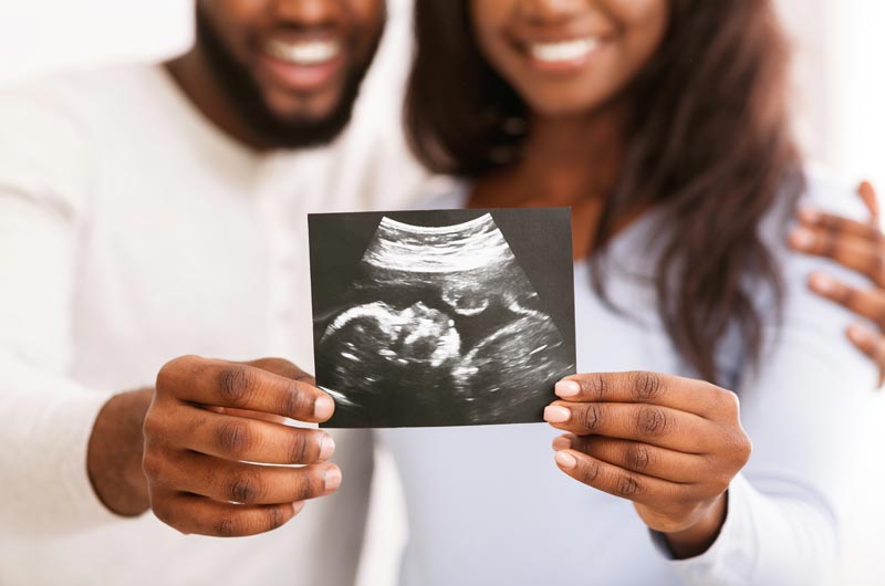 smiling african american couple showing ultrasound